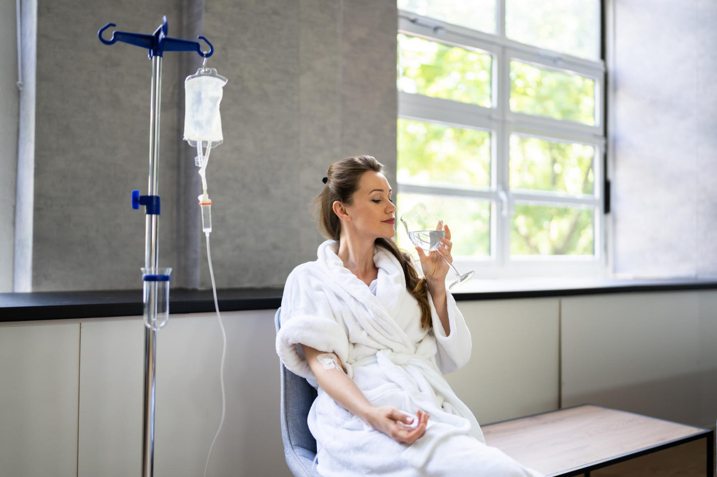 Woman in a hospital room with an IV stand and a window in the background