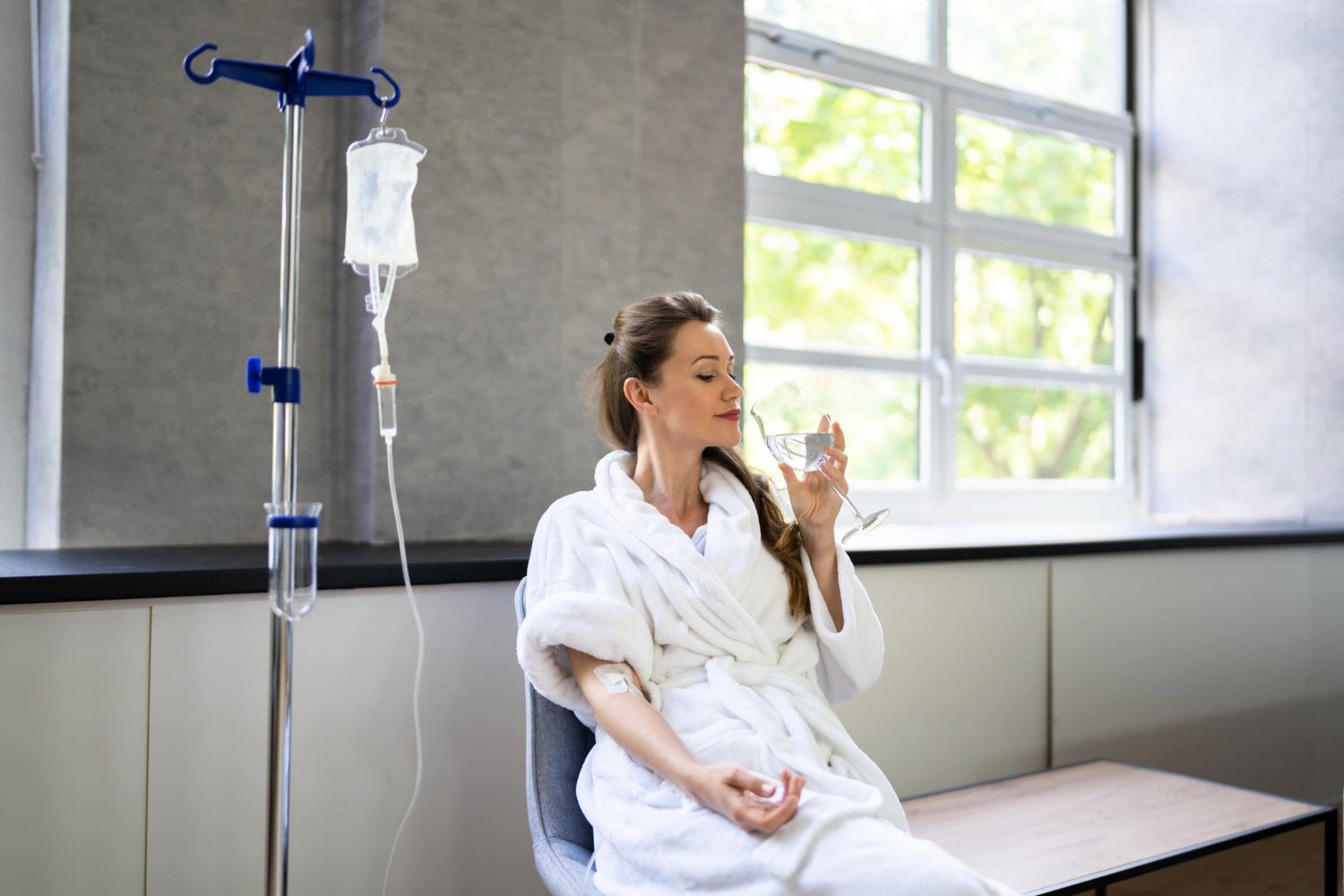 Woman in a hospital room with an IV stand and a window in the background