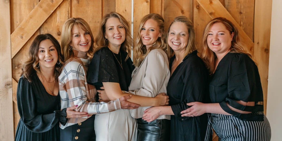 Group of six women posing together in a wooden interior setting