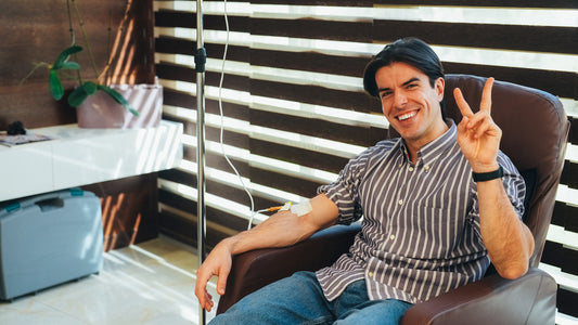 Man sitting in a chair making a peace sign in an indoor setting with striped wall and plant.